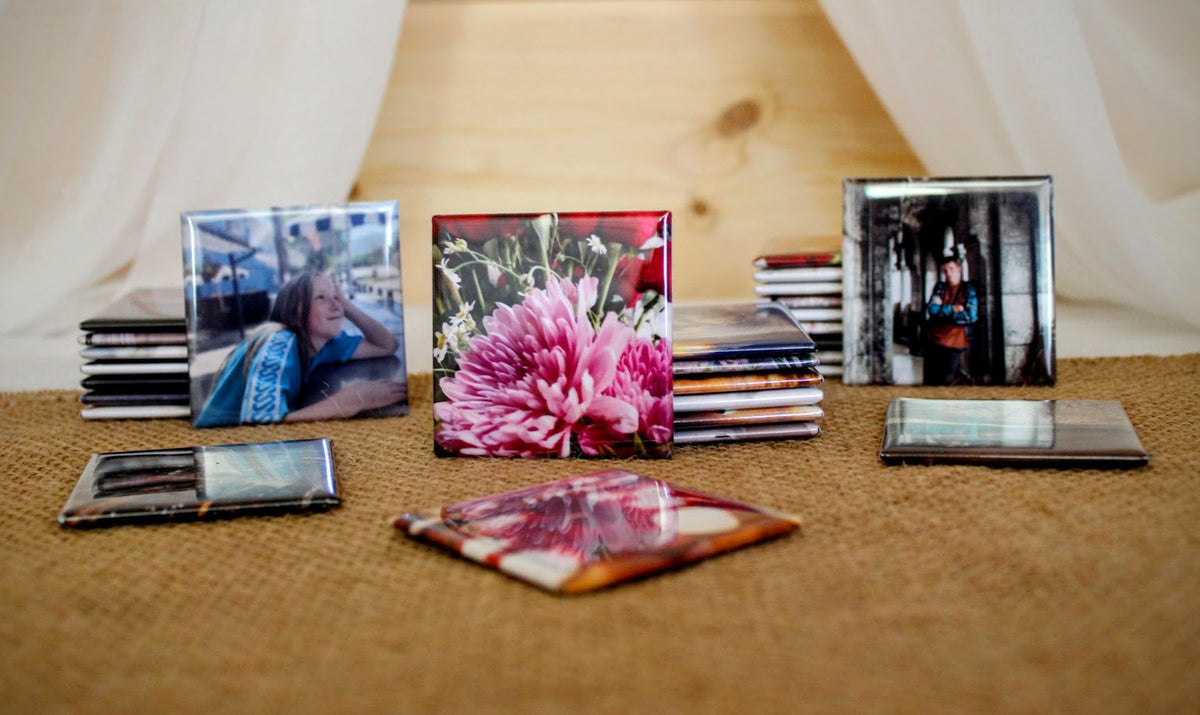 A collection of custom photo tiles and CD jewel cases arranged on a burlap surface in front of a wooden backdrop with draped fabric.